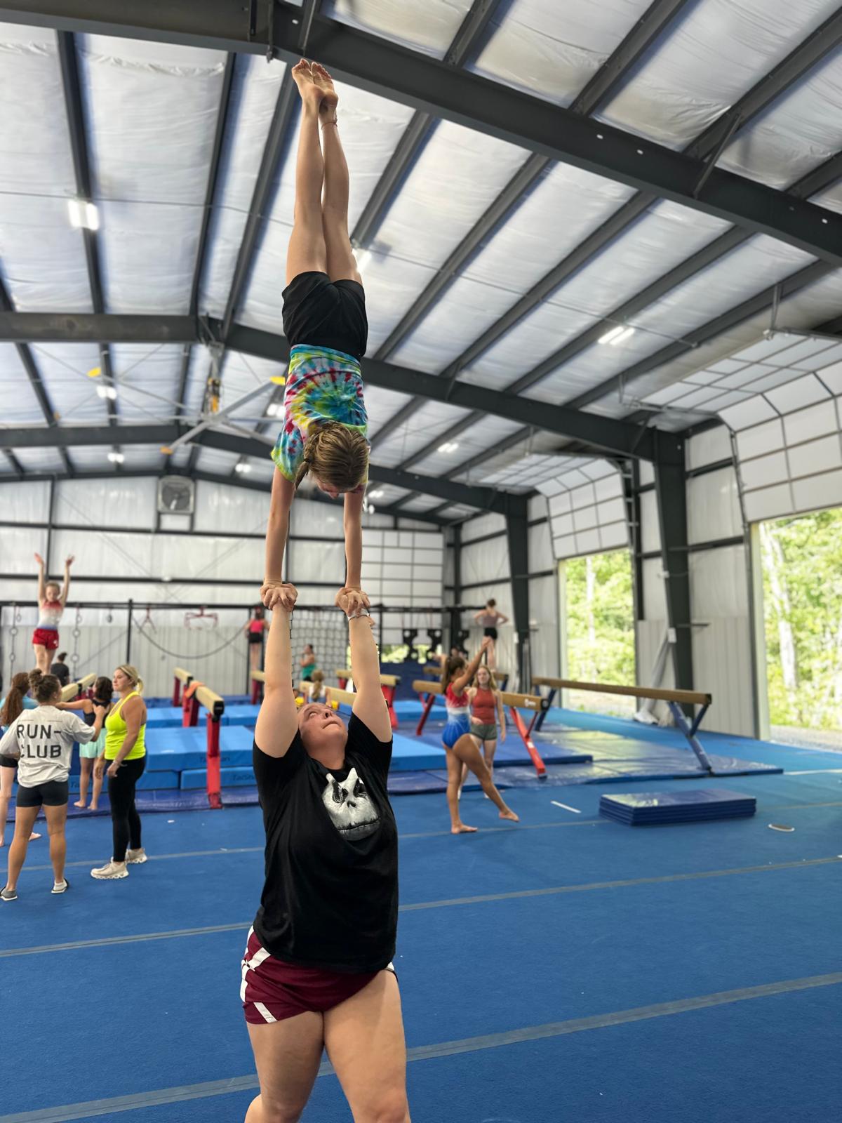 girl doing handstand with coach in gymnastics gym